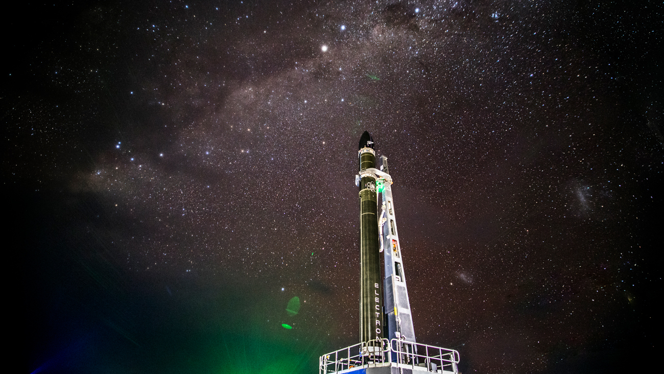 a black rocket stands on the launch pad under a starry night sky.