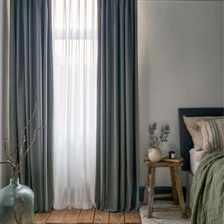 a small bedroom with grey full length curtains hung over the window