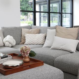 Grey sofa with light coloured cushions, wood tray table, vase, lamp
