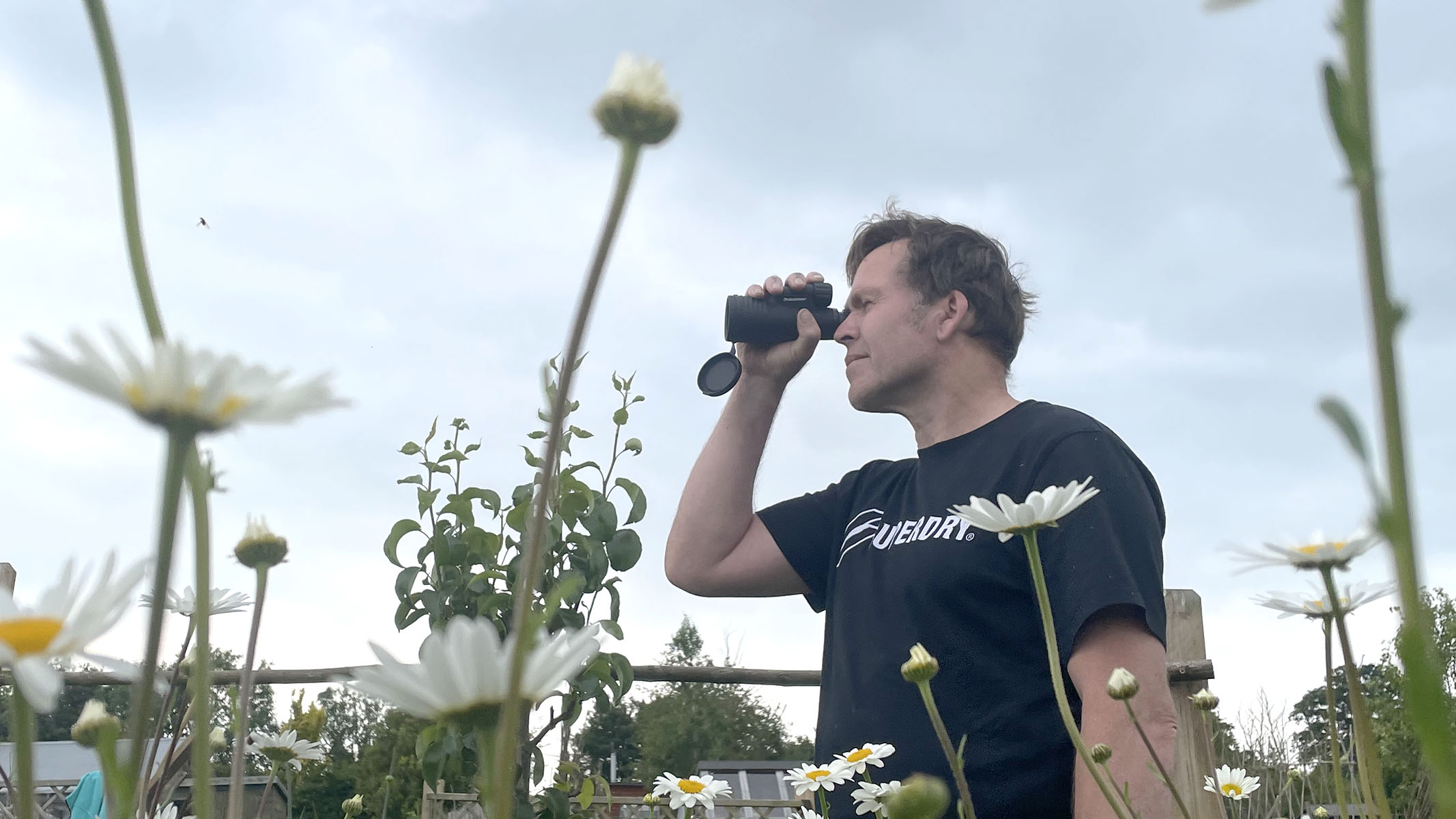 A Celestron Outland X 10x50 monocular in use in a field of daisies.