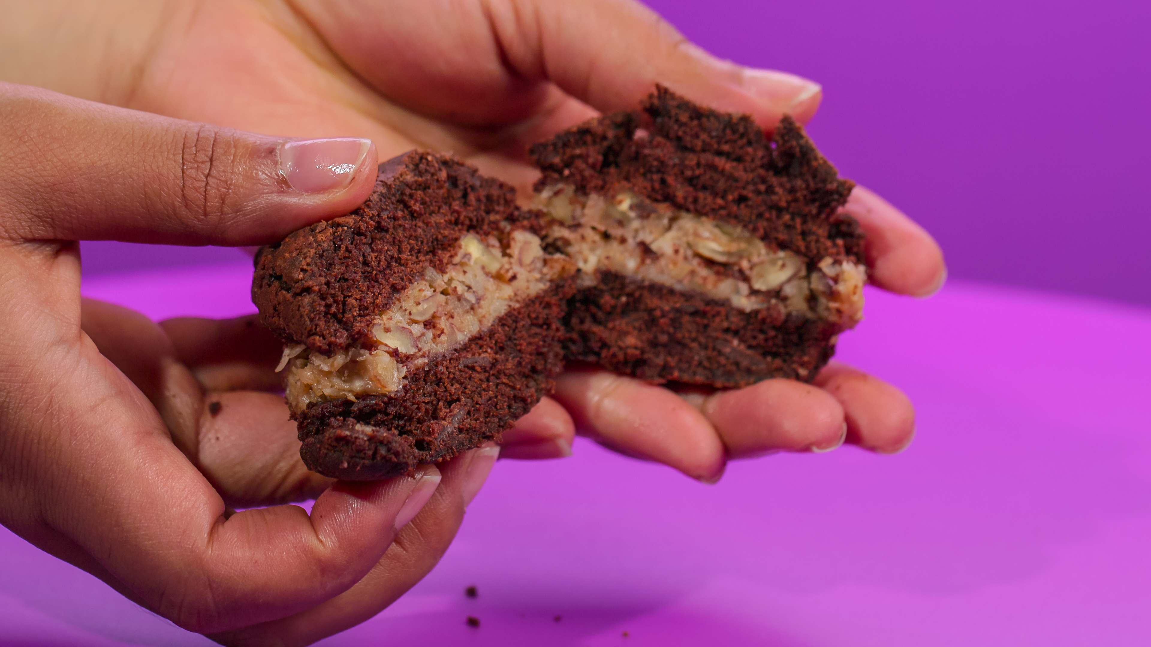 A hand holds a chocolate cream filled dessert split in half in SNACK vs.  CHEF