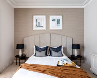 A neutral bedroom with curved grey headboard and rust-colored throw