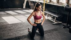 Woman wearing sportswear kneels on gym floor with her hands on her hips