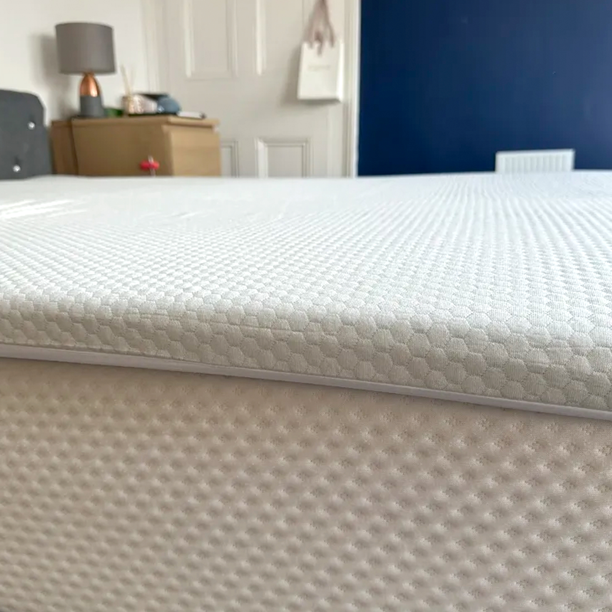 The Panda Topper being tested on top of a mattress on a grey upholstered bed in a bedroom