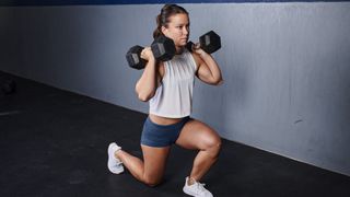 Woman performing lunge holding two dumbbells by her shoulders