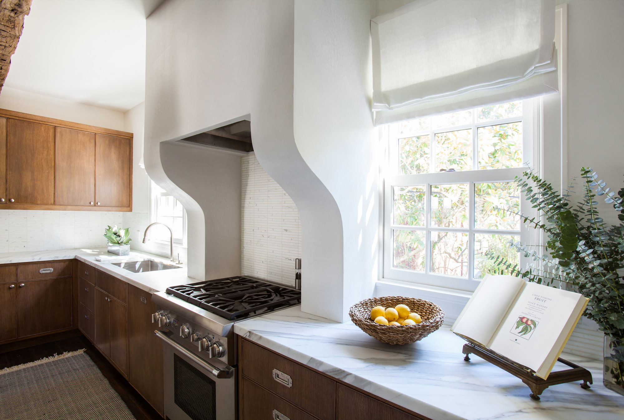 A kitchen with wooden cabinetry, marble countertops, and a curved, built-in plaster hood