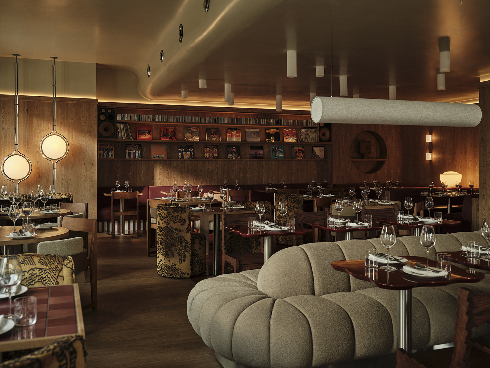 A modernly furnished restaurant with a nod to the 1980s' music charm, with oversized cream couches, wood, tile, and chrome tables, spherical warm lighting, sculptural ceilings, and pendant lights, as well as a records-filled wall.