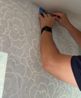 Dori Turner trimming the top of the peel and stick wallpaper with utility knife