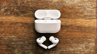 AirPods Pro 2 ligger på et træbord ved siden af opladningsetuiet