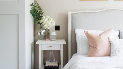 Neutral bedroom with white sheets on bed and vase on table