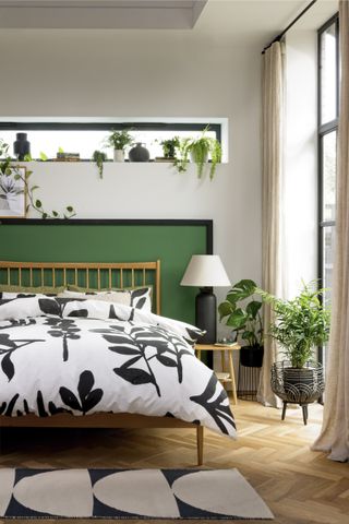 bedroom with green painted feature headboard, lots of plants and monochrome botanical bedding