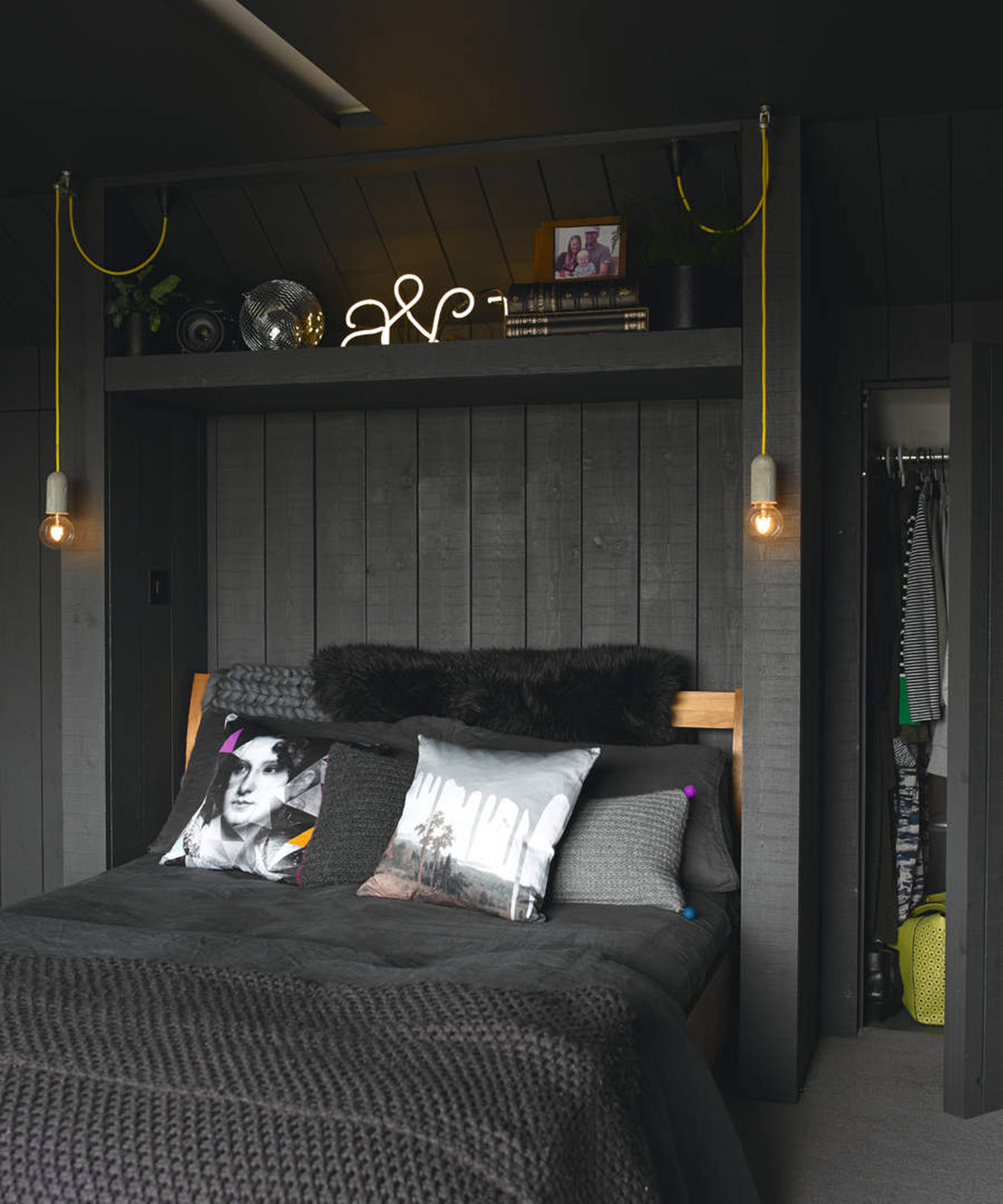 A loft bedroom with wall paneling and black wall paint decor with above bed shelving