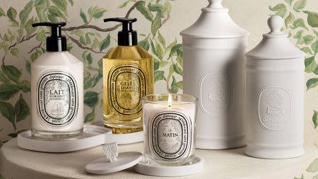 Diptyque Les Rituels de Soin collection on a white table with white wallpapered walls with vines