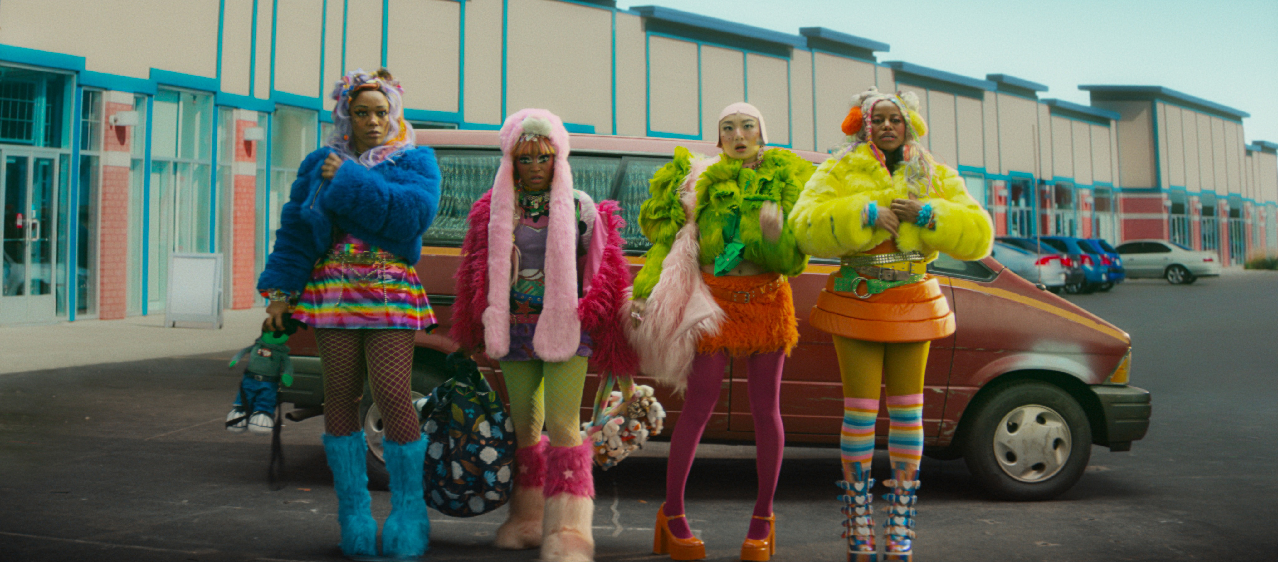 Naomi Ackie as Sade, Keke Palmer as Corvette, Poppy Liu as Jianhu, Taylour Paige as Mariah wear eccentric colorful outfits while standing in a parking lot in front of a car, in 'I Love Boosters'