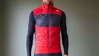 A male cyclist wearing a red Castelli Unlimited Puffy vest 