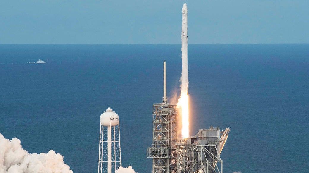 a white spacex falcon 9 rocket launches with the ocean and a blue sky in the background.