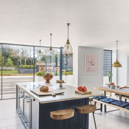Open plan kitchen diner with navy units and island, pendant lights and large sliding patio doors