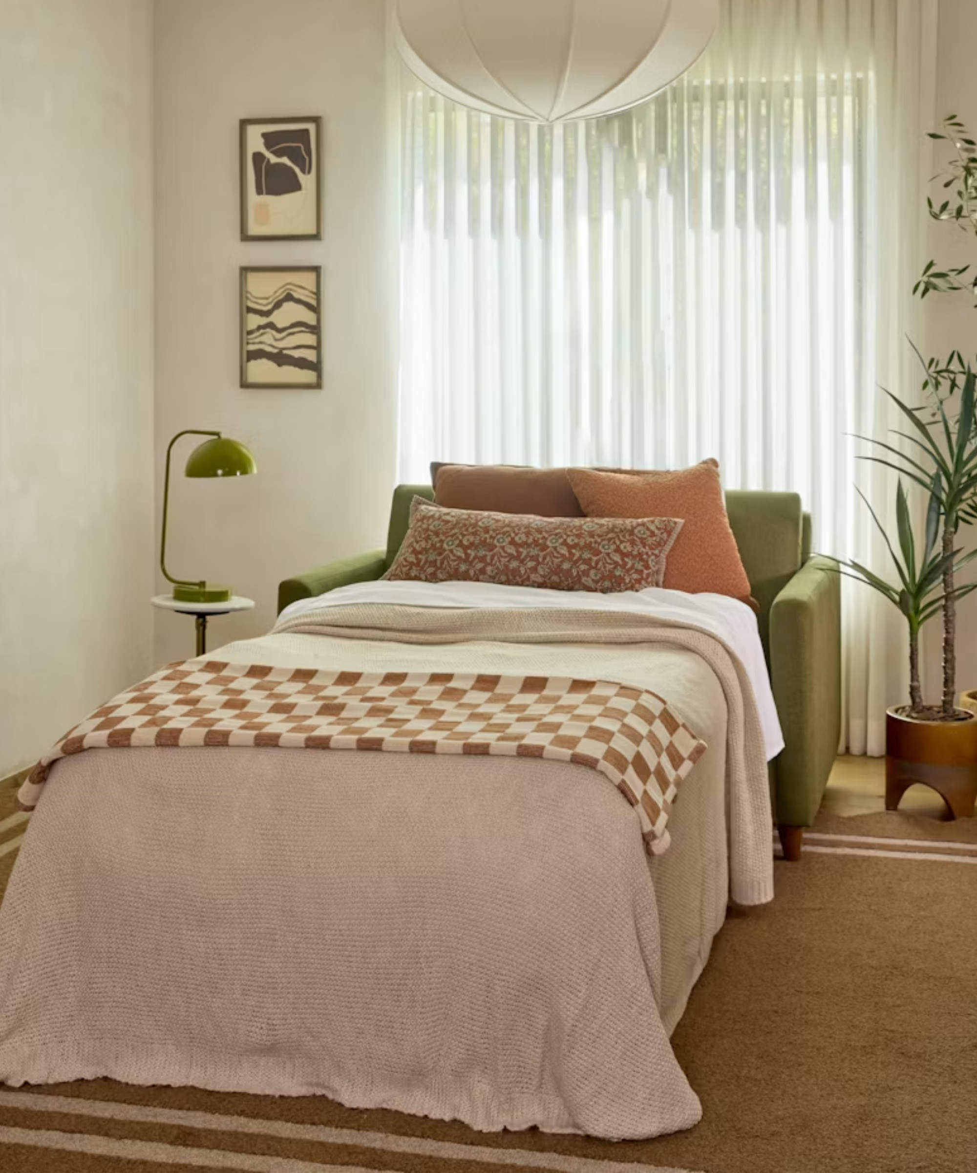 Twin-sized green sleeper sofa styled in a small, eclectically decorated living room with sheer draped and a fabric pendant light.