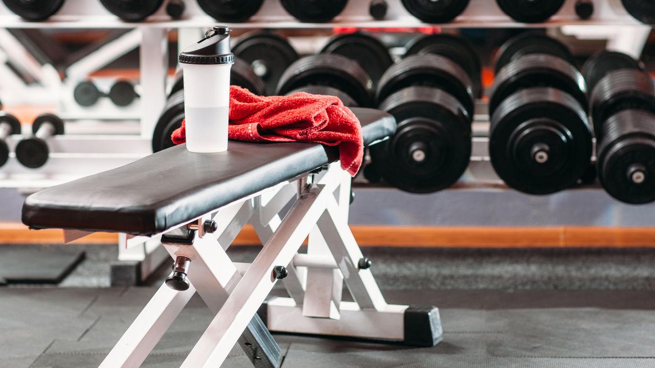 The best ab machine: ab bench in gym next to weights with red towel on top and water bottle