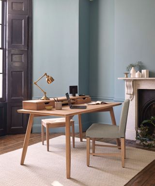 blue home office with fireplace, natural wooden desk and chair and table lamp