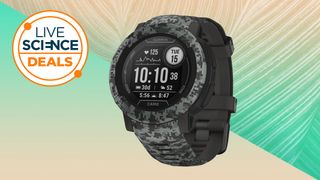 A Garmin Instinct 2 smartwatch on a green/light brown background with a Live Science deals icon