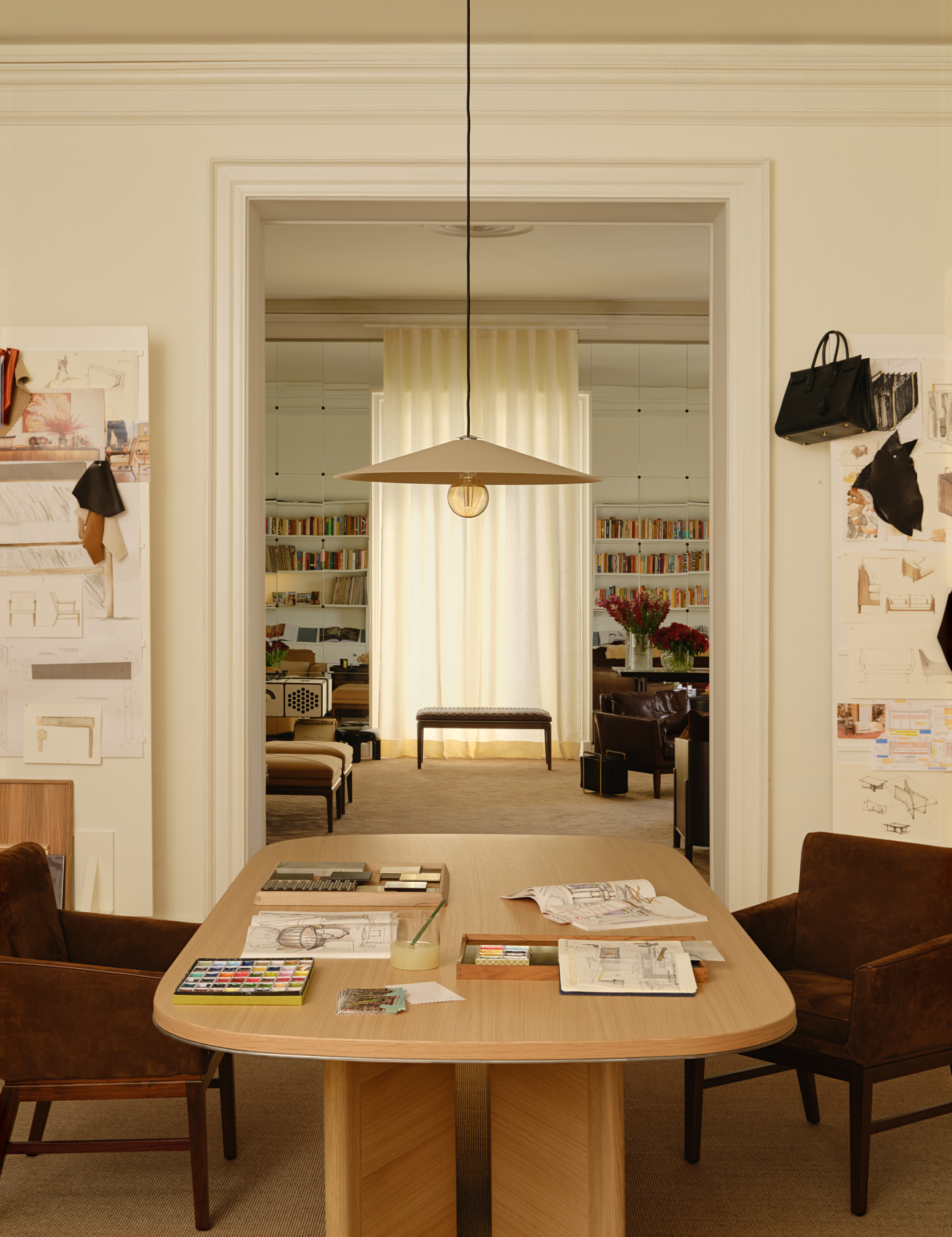 Eclectic art-filled dining room area highlighting the making of GACHOT by Artemest with sketches and swatches pasted to the walls and sprawled across the stately oak wood dining table