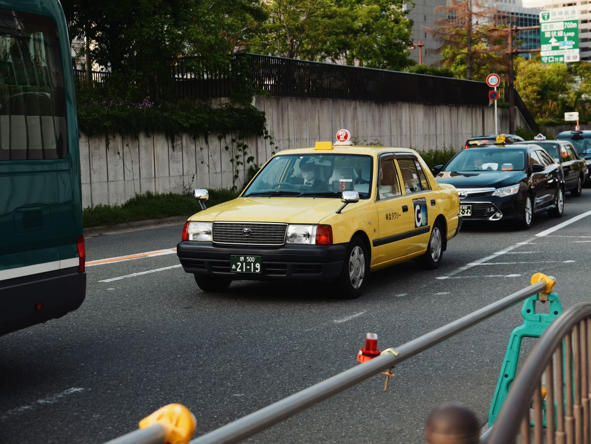 Yellow taxi driving through traffic on an Osaka street.