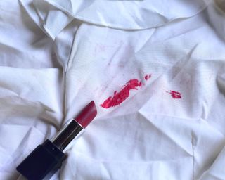Red lipstick makeup stain on white clothes with lipstick capsule in shot