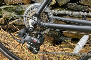 The Brand X Road Bike cassette and rear Shimano Tourney rear mech shown on the damp bike in front of a stone wall and yellow grass