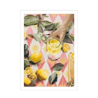 A wall art watercolor print of a pink argyle patterned table with green leaves, lemons, and a hand holding a glass of yellow lemonade