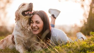 Woman laying on grass cuddling her dog