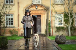 Women in tweed holding a shotgun next to a white lab