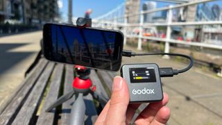 Godox Magic XT1 microphone held in a hand in front of an iPhone on a tripod