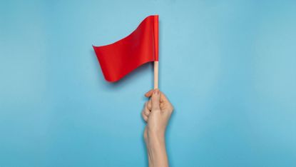 Hand holding a small red flag against a blue background