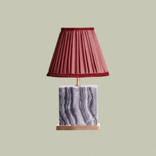 A table lamp with a marble base and a red pleated shade