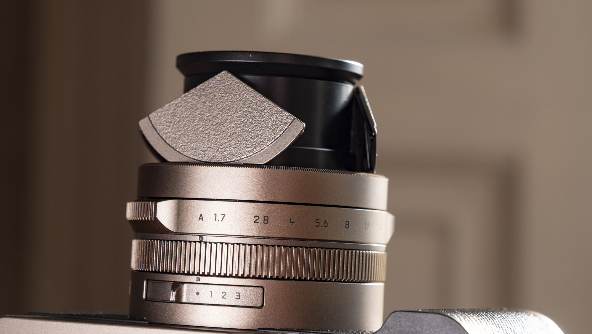 Close up of the lens of the Titanium Gold special edition of the Panasonic Lumix L10 compact camera, on an antique wooden table 