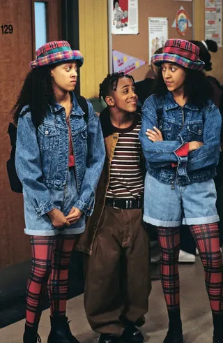 Tia and Tamara wearing a plaid bucket hat, red plaid tights, a denim jacket, and jean shorts.