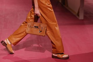 Detailliertes Bild von Hermes-Models, die in Lederhosen und Clogs über den Laufsteg der Frühjahr/Sommer-Kollektion 2025 laufen