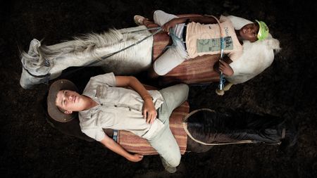 Two boys lie on horses in relaxed poses on a dark ground