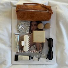 Beauty products and miscellaneous items spread out on a newspaper on a bedspread.