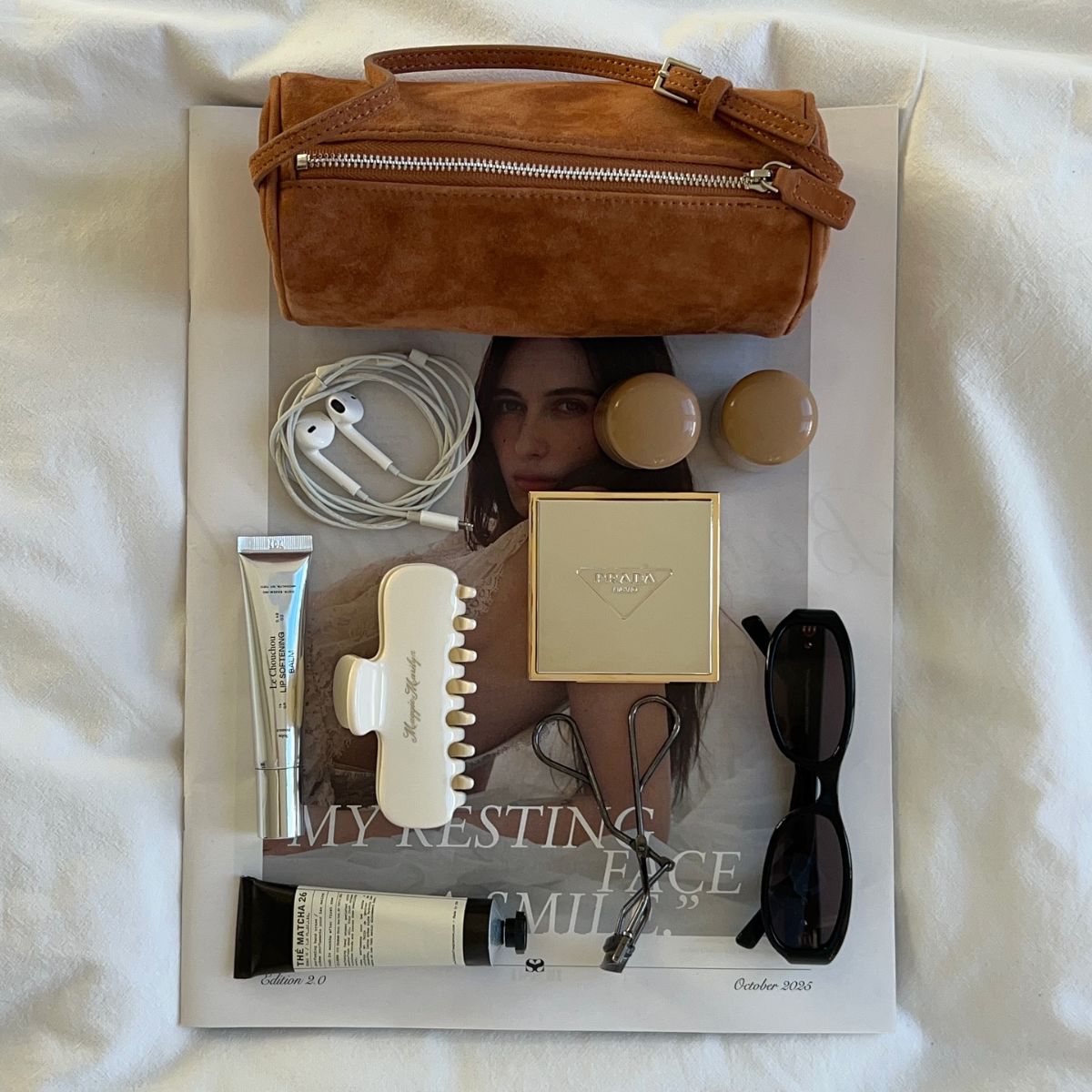 Beauty products and miscellaneous items spread out on a newspaper on a bedspread.