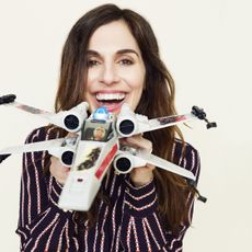 Michelle Rejwan smiles as she holds a toy X-Wing up to the camera