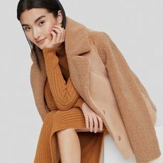 Woman wearing Nordstrom Rack knitted tan dress and teddy coat with gold earrings.