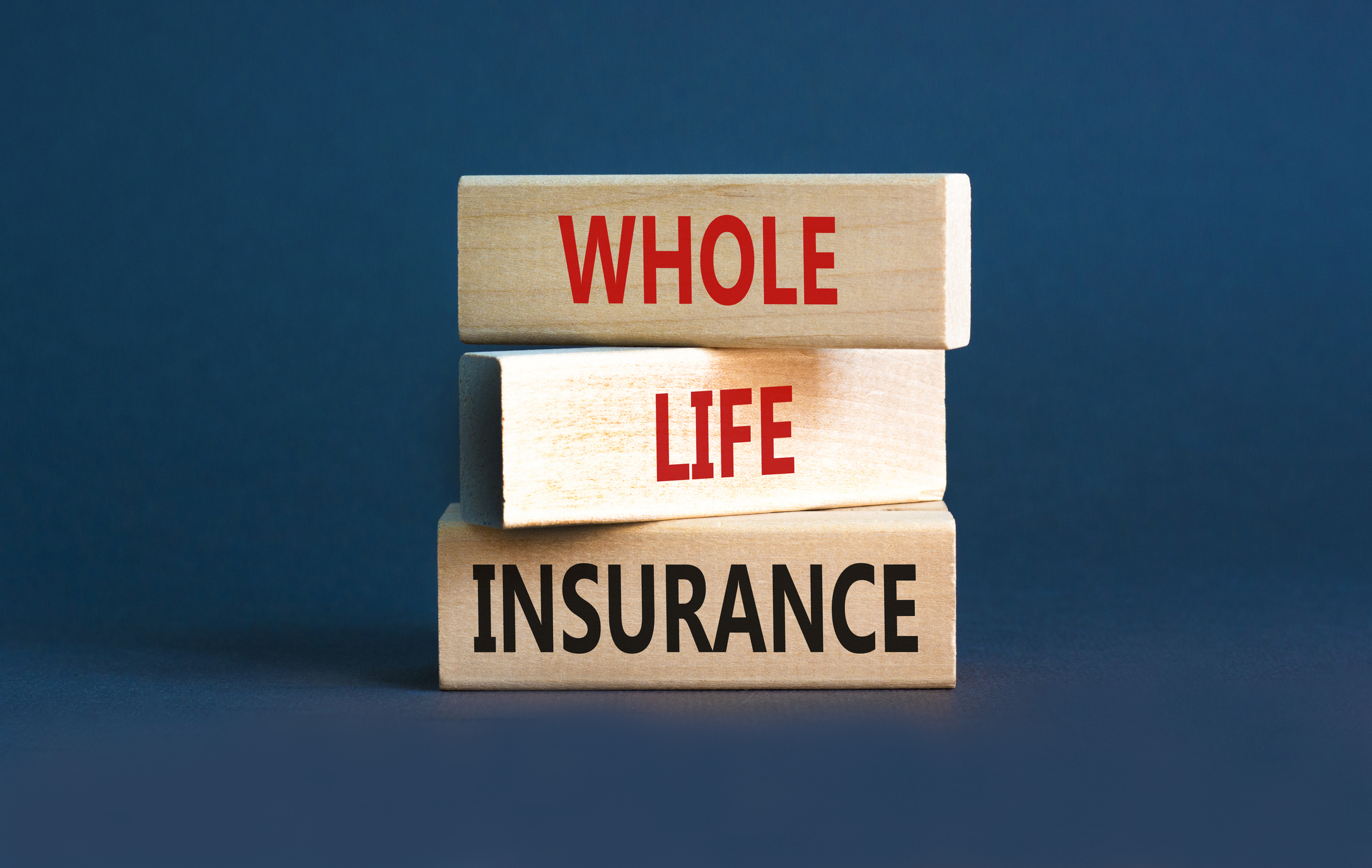 Three wooden blocks agaisnt a blue blackground. Each block has a word on it, spelling out "whole life insurance."