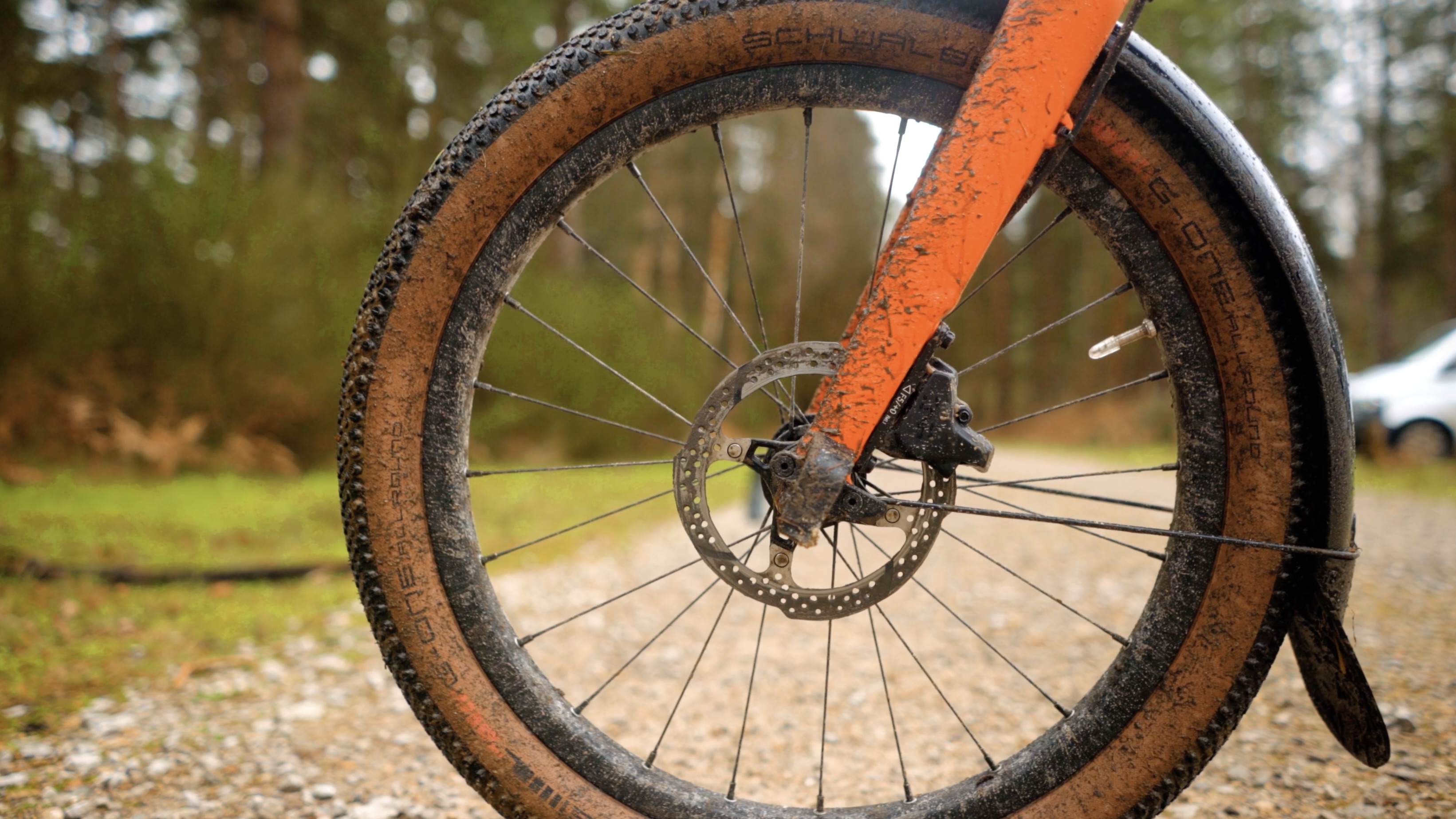 An orange Brompton covered in mud on a light gravel track