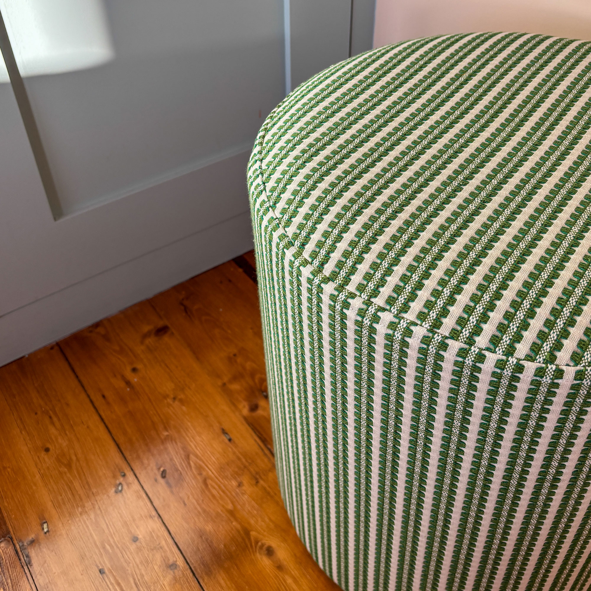 Green and white striped fabric pouffe on wooden floor