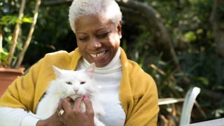 A senior woman sits in the garden cuddling a beautiful white cat.