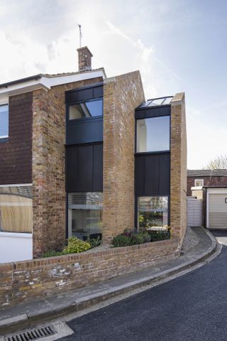 Modern extension to the side of a house, with black panels above and below windows, with the road in the foreground of the picture