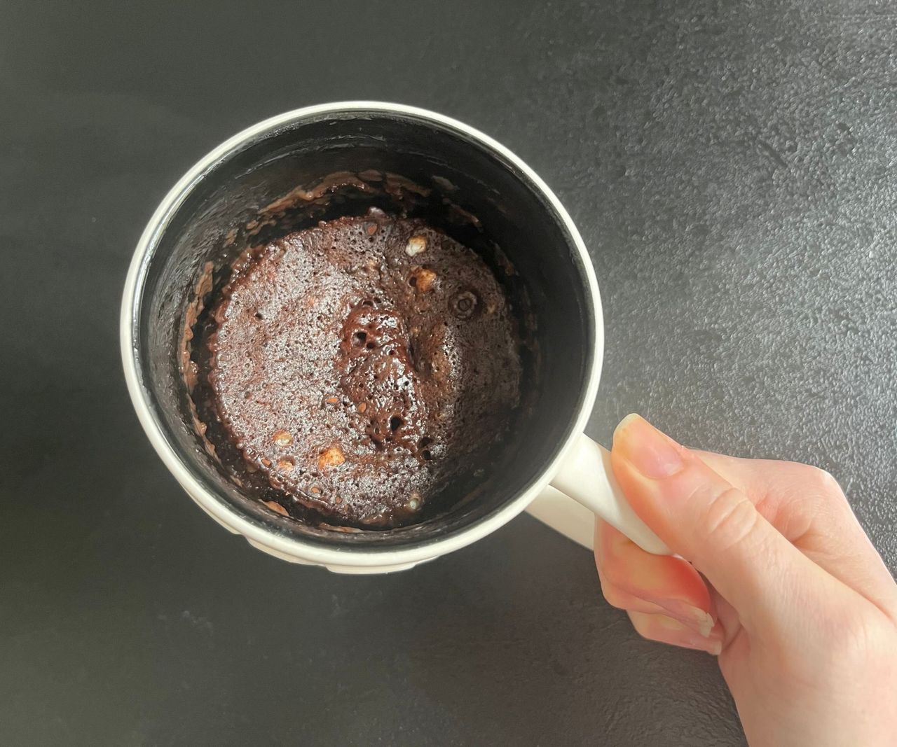 A white mug on a black counter with a chocolate cake inside