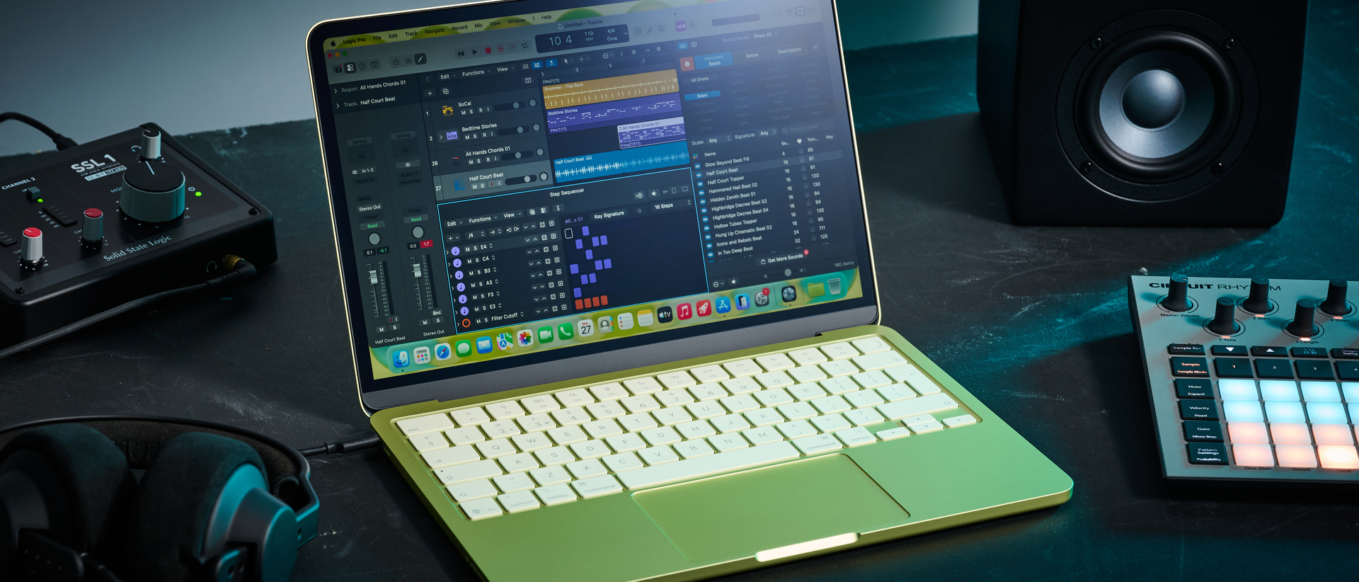 An Apple MacBook Neo laptop on a desk with an audio interface, studio monitors, headphones, and a MIDI controller